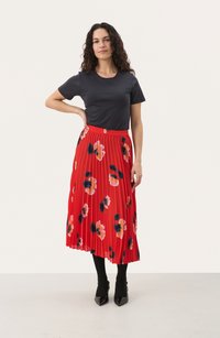 Rød plisseret nederdel med blomstermønster, parret med en sort t-shirt. Nederdelen har levende farver og blødt stof. Bæres med sorte strømpebukser og hæle.