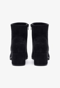 Mustroorilised mustad nahast ankle boots ümarate varvastega, kahe külgse lukuga, ruudukujulise kanna ja siledat tekstuuri, nähtud tagant.