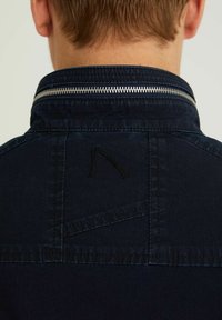 Navy blue jacket with a high collar and silver zipper. Features a subtle embroidered logo and visible stitching details on the back.