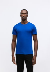 T-shirt blu a maniche corte realizzato in cotone liscio, con scollatura rotonda e silhouette aderente, abbinato a pantaloni neri.
