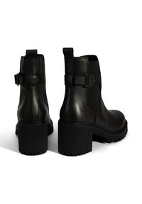 Bottines en cuir noir avec des talons en caoutchouc épais, des panneaux latéraux élastiques et un accent de boucle sur les côtés extérieurs. Design texturé et robuste.