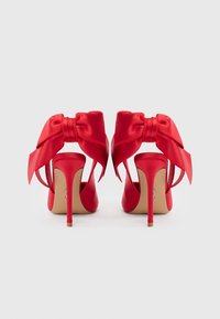 Røde satin h�øje hæle med en stor sløjfe på bagsiden, åbne sider og en slank stilet hæl. Glat tekstur med en blank finish.