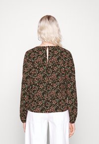 Blouse florale noire avec manches longues, détail en forme de goutte dans le dos et motif floral multicolore sur un tissu doux.
