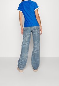 Blå mönstrad T-shirt med vit kant som matchas med lösa, ljusblå jeans med grafiska mönster och text. Avslappnade skor fulländar looken.