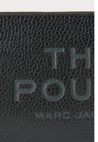 Surface en cuir noir texturée avec des lettres noires en relief épelant "TH POU" et "MARC JAC" en plus petit partiellement visibles en dessous.