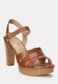 Hnedé kožené platformové sandále s vysokým blokovým opätkom, viacerými prekríženými remienkami a zapínaním na pracku. Textúrovaná podošva pripomínajúca drevo pre lepšiu priľnavosť.