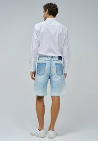 Shorts de mezclilla de color azul claro con un lavado desgastado, que cuentan con dos bolsillos traseros, costuras amarillas como acento y un corte relajado, combinados con una camiseta blanca.