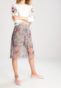 Top gris de manga larga con bordado floral en las mangas, combinado con una falda plisada y transparente de flores y zapatillas de lona rosas.