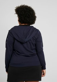 Navy modrá mikina s kapucí vyrobená z bavlněné směsi, s tkaničkami na kapuci, žebrovanými manžetami a slim fit střih, doplněná černou sukní.