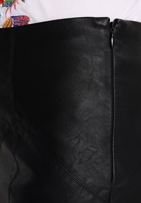 Gonna a matita in pelle nera con una superficie liscia, cuciture in vista e zip laterale. Il design presenta una silhouette aderente con cuciture angolari.