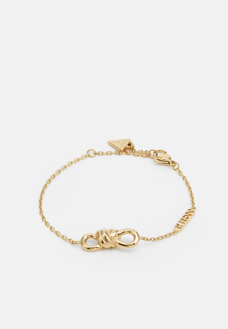 Gold chain bracelet with a sleek, twisted knot centerpiece and a small triangular tag. Engraving reads "CUBISM" on one link.