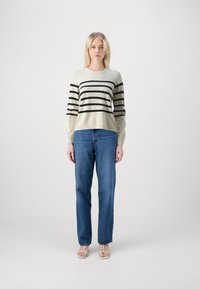 Leichter, cremefarbener Pullover mit schwarzen horizontalen Streifen, kombiniert mit blauen geraden Jeans und hellen, schnüren Sandalen.