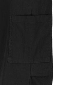Schwarzer Stoff mit einem großen Taschen-Detail, das saubere Nähte und eine glatte Textur aufweist. Das Design betont Minimalismus und Funktionalität.