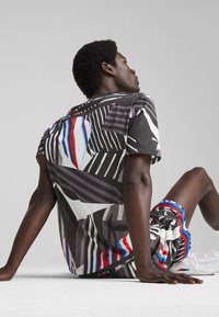 Męski zestaw odzieży sportowej z czarną, wzorzystą siatkową koszulką oraz szortami z czerwonymi, białymi i niebieskimi akcentami, prezentującymi geometryczny wzór.