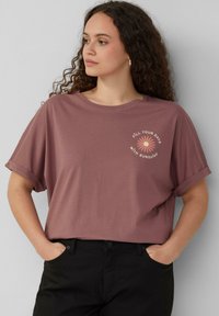 Korte mouwen, mauve t-shirt met opgerolde mouwen en een bloemenafbeelding met de tekst "VUL JE DAGEN MET ZONNESCHIJN." Zacht katoenen materiaal.