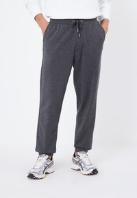 Graue Sweatpants mit einem Kordelzugbund, seitlichen Taschen und schmal zulaufenden Beinen, kombiniert mit grauen und weißen Sportschuhen.