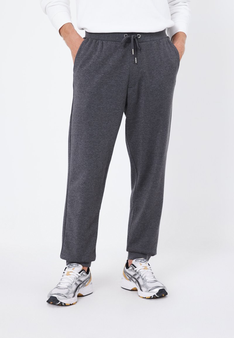 Graue Sweatpants mit einem Kordelzugbund, seitlichen Taschen und schmal zulaufenden Beinen, kombiniert mit grauen und weißen Sportschuhen.
