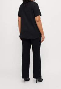 Zwarte top met korte mouwen, een gebogen zoom en een sleutelgat aan de achterkant, gecombineerd met zwarte flare pants en gesloten hakken.