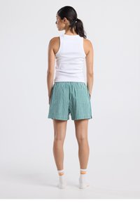 Valkoinen hihaton paita yhdistettynä vihreisiin ja valkoisiin ruudullisiin shortseihin. Shortseissa on joustava vyötärönauha, ja jaloissa oranssiraitaiset sukat.