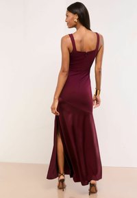 Pügav burgundia suurustes kleit, millel on sobiv büst, laiad rihmad ja reie kohal lõhiku. Sile kangas koos kerge säraga ja seljaosal tõmblukuga detail.