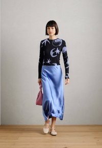 Μαύρο μπλουζάκι με μακριά μανίκια και μωβ αφηρημένα σχέδια, συνδυασμένο με μια ανοιχτόχρωμη μπλε σατινέ μίντι φούστα. Τα αξεσουάρ περιλαμβάνουν μια ροζ τσάντα και ανοιχτόχρωμα παπούτσια.