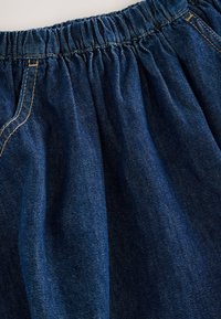 Dunkelblauer Denimstoff mit einem gerafften Bund, sichtbaren Nähten und weicher Textur. Geeignet für legere Kleidung oder den Gebrauch zu Hause.