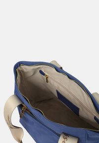 Borsa in nylon blu con interno beige. Presenta una chiusura con zip, tasca interna e manici crema. Include dettagli in metallo dorato.