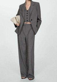 Abito grigio a righe sottili con giacca doppiopetto, top corto abbinato con bottoni e pantaloni a gamba larga, abbinato a una clutch beige.