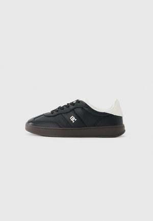 Czarny niski sneaker z brązową podeszwą, czarnymi sznurowadłami, białym kołnierzem przy pięcie oraz małym białym logo z boku.