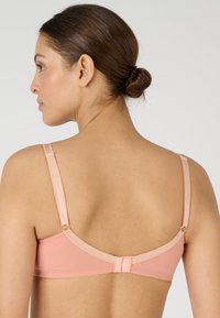 Reggiseno rosa chiaro con spalline regolabili, tessuto morbido, chiusura con gancio e design senza cuciture. La vista posteriore mostra una trama uniforme e dettagli minimi.