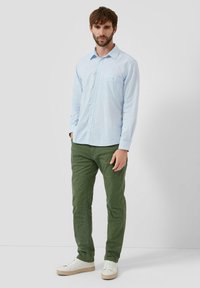 Jasnoniebieska koszula z długim rękawem i kieszenią, zestawiona z oliwkowozielonymi spodniami oraz białymi trampkami. Materiał wydaje się gładki i casualowy.