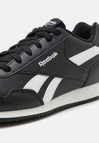 Sneaker in pelle nera con accenti bianchi, caratterizzato da una superficie testurizzata, punta rotonda, lacci neri piatti e suola in gomma bianca.