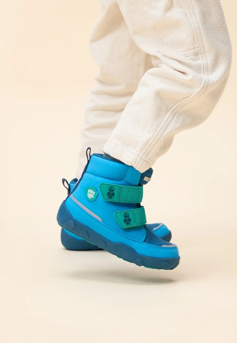 Botas de invierno de color azul brillante con correas ajustables verdes, tejido texturizado, suelas de goma y detalle de logo en el costado. Acolchadas para mayor comodidad y calidez.