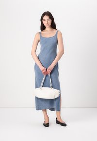 Denim maxi šaty s tenkými ramienkami, modrá farba, bočné rozparky, v kombinácii s bielou kabelkou. Čierne ploché topánky dotvárajú vzhľad.