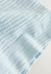 Helehall sinine kangas vertikaalse soonilise kudumistruktuuriga, mis näitab pehmeid voldikuid ja peeneid õmbluse detaile.