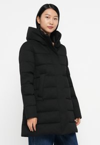 Piumino nero con colletto alto, caratterizzato da un design trapuntato orizzontale, due tasche laterali e chiusura con zip. Tessuto liscio.