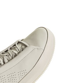 Ljusgrå sneaker med en slät läderöverdel, lågt snitt, rund tå, snörning och perforerat detaljer på sidan.