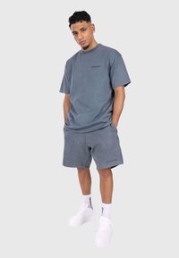 Grå bomulds t-shirt med løs pasform og korte ærmer, parret med matchende grå shorts. Hvide sneakers og sokker med branddetaljer.