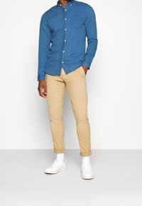 Blå knapp-up skjorta med bröstficka, parat med beige chinos och vita sneakers. Skjortan har en texturerad yta och långa ärmar.