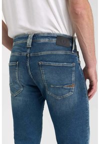 Pantalones vaqueros de algodón en azul medio con un acabado desgastado. Cuenta con una cinturilla, dos bolsillos traseros y un parche de cuero con el logo en la parte posterior.