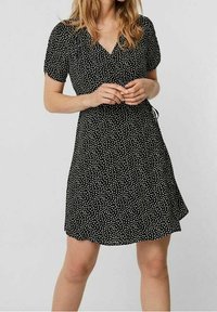 Schwarzes Kurzkleid mit V-Ausschnitt, kurzen Puffärmeln und einem verstreuten weißen Punktmuster. Weicher Stoff mit einer luftigen A-Linie-Silhouette.