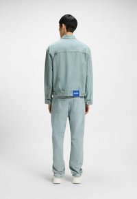 Light blue denim jacket and matching jeans. Jacket features a classic collar, button closure, and logo patch on the back.