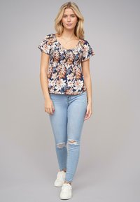 Bloemtop met een marineblauwe achtergrond, korte mouwen, en een geraffineerde halslijn; gecombineerd met lichtblauwe ripped skinny jeans en witte sneakers.
