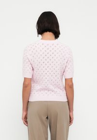 Pull tricoté à manches courtes de couleur rose clair avec motif ajouré, poignets et ourlet côtelés. La vue de dos montre un motif texturé et une silhouette ajustée.