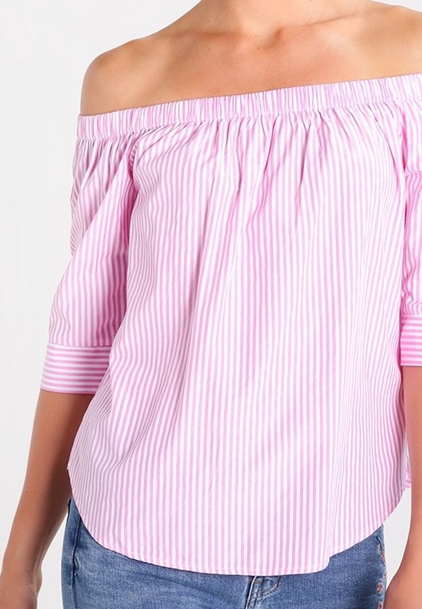 Femme portant un chemisier à rayures verticales rose et blanc, épaules dénudées et manches trois-quarts, associé à un jean en denim bleu.