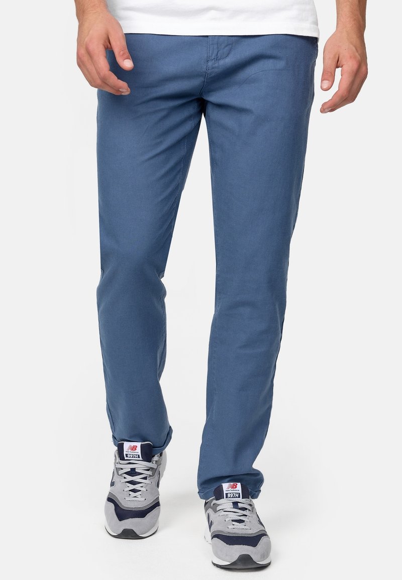 Pantalon en coton bleu clair à coupe droite, avec poches latérales et texture lisse. Associé à des baskets grises.