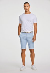 Vit kortärmad T-shirt matchad med ljusblå rutiga shorts, uppvikt ärm, och ett brunt bälte, komplett med vita sneakers.