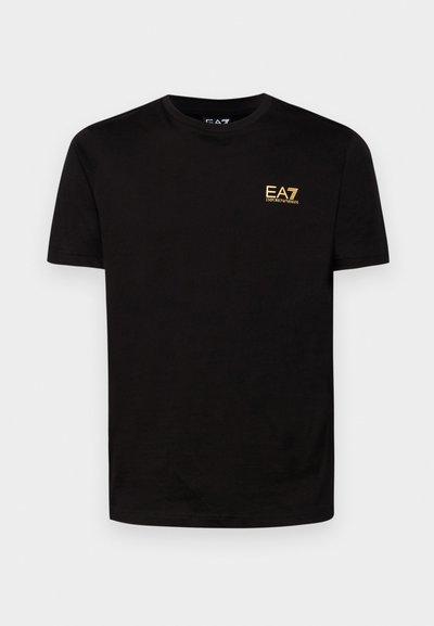 T-shirt en coton noir à manches courtes, col rond, avec un logo EA7 brodé jaune sur la poitrine gauche. Texture lisse.
