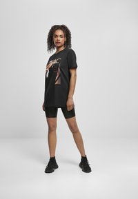 T-shirt noir avec un imprimé graphique représentant 2Pac, associé à un short de vélo noir et des chaussures de sport noires. Le tissu semble doux et décontracté.