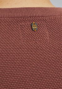 Bordeaux gestrickter Pullover mit einem strukturierten Muster. Verfügt über ein schwarz-orangefarbenes Etikett mit der Aufschrift "PME Legend", das sich am hinteren Halsausschnitt befindet.